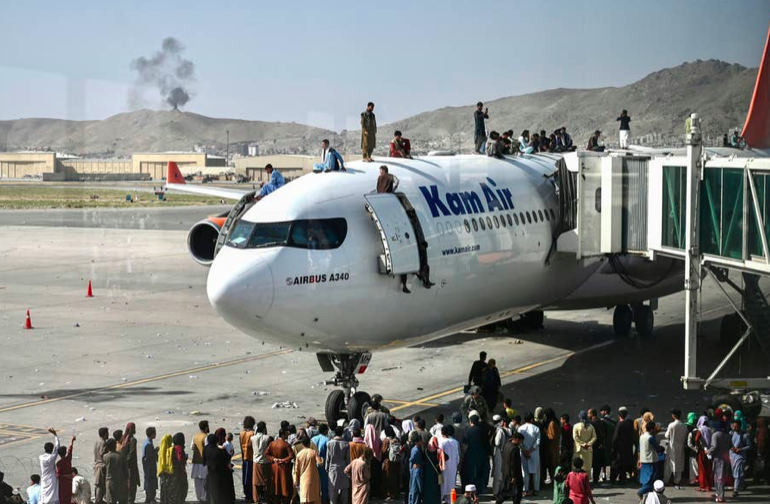 Afghan people climb atop a plane as they wait at the Kabul airport