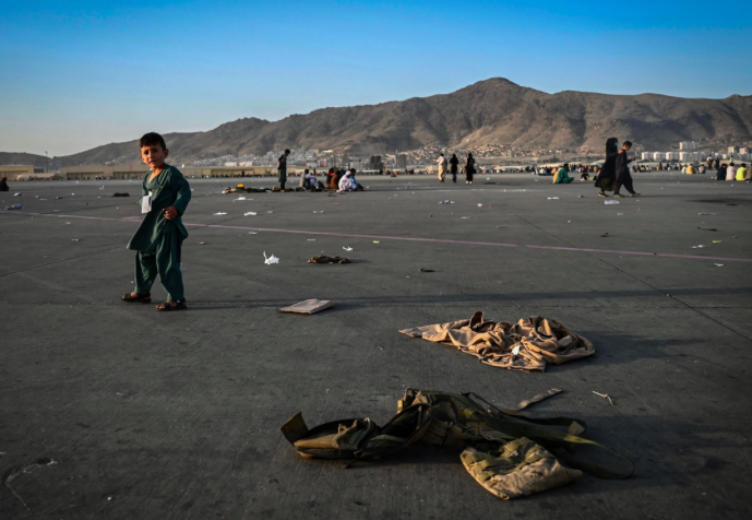 Afghan child waits to leave Kabul on the tarmac of the airport near military uniform